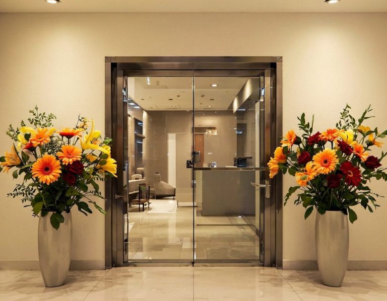 b2b Blumen für Büro und Unternehmen Eingang mit Glastüren, verziert mit bunten Blumenarrangements auf beiden Seiten.