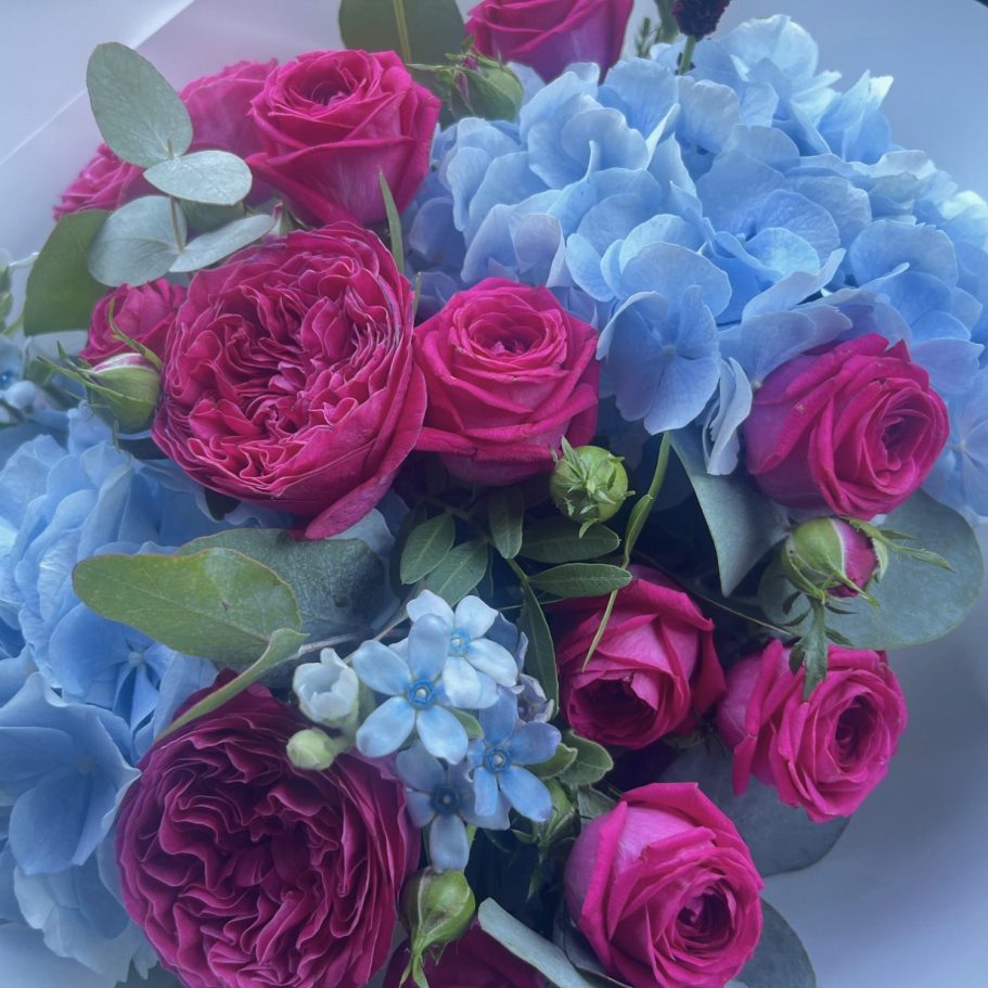 Geburtstagsstrauß vom Floristen in Steinhagen Bunter Blumenstrauß in einer Glasvase mit rosa und lila Blüten, umgeben von grünen Blättern.